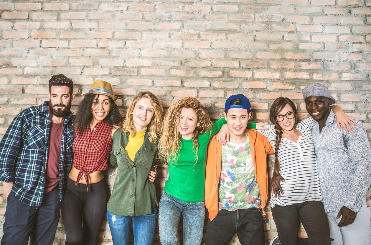 Group portrait of multi-ethnic boys and girls with colorful fashionable clothes holding friend in hands and posing on a brick wall - Urban style people having fun, studio shot - Concepts about youth and togetherness
